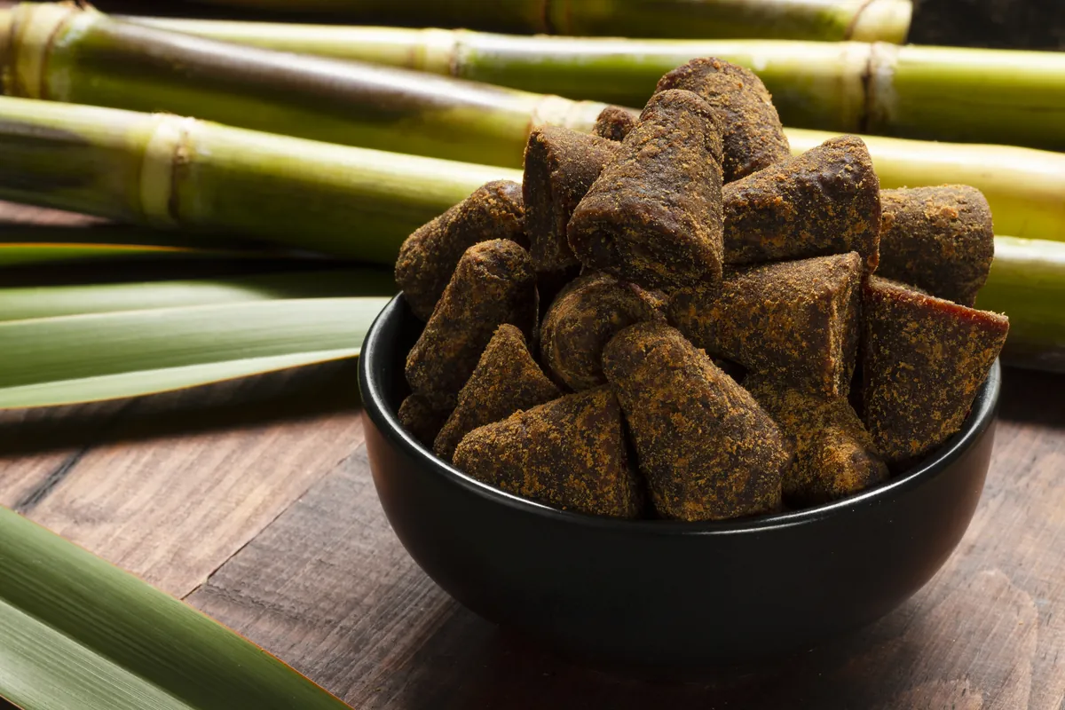 Dark jaggery blocks in a bowl with sugarcane stalks