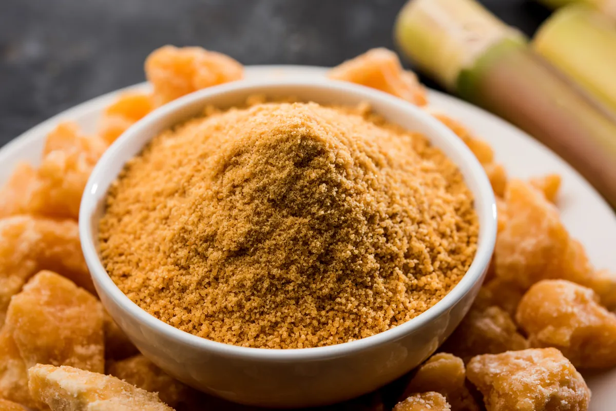 Bowl of jaggery powder beside jaggery lumps and sugarcane