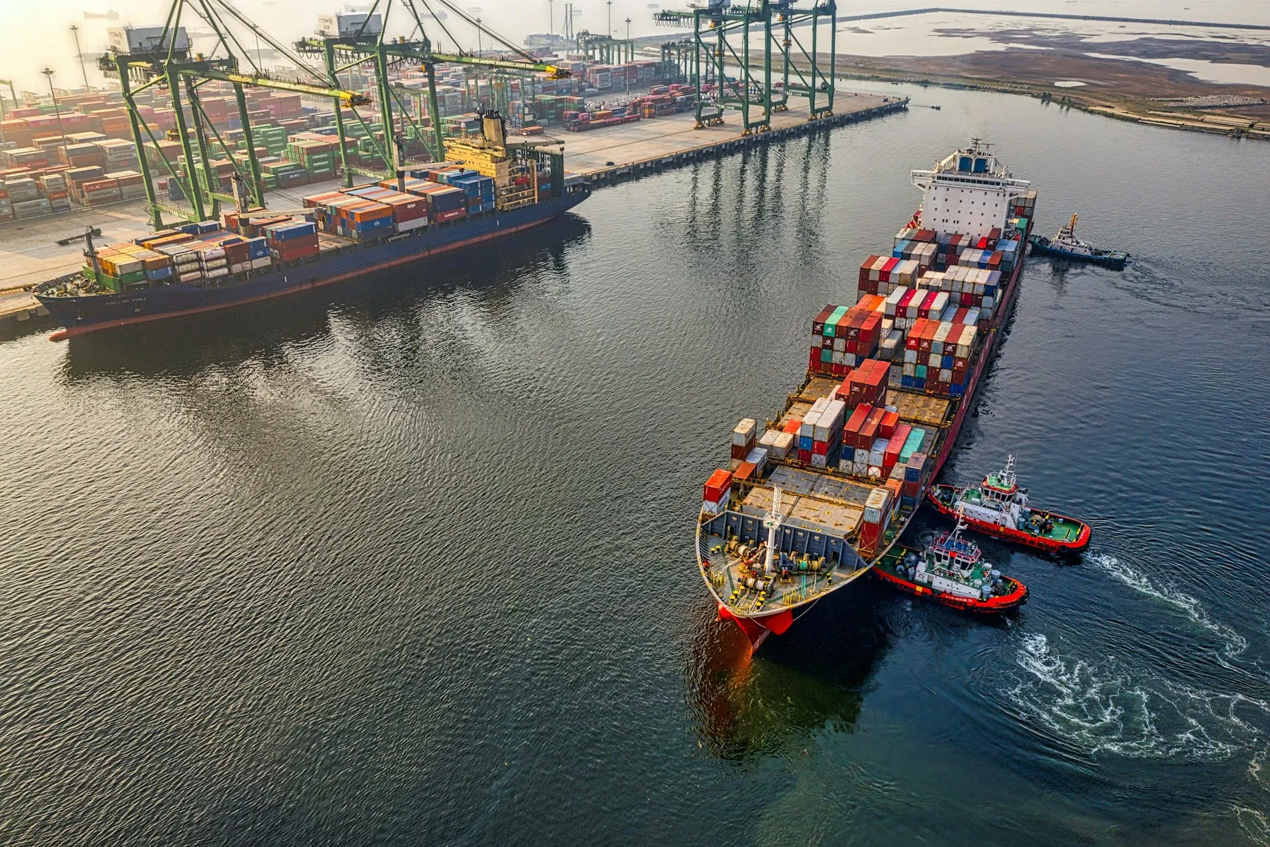 Container ship guided by tugboats into a port berth